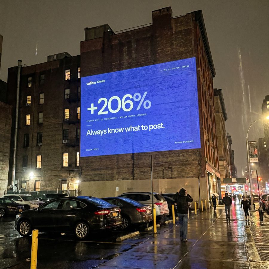 Willow Create-projectie op een gevel bij nacht met de tekst '+206% — weet altijd wat je moet posten.'