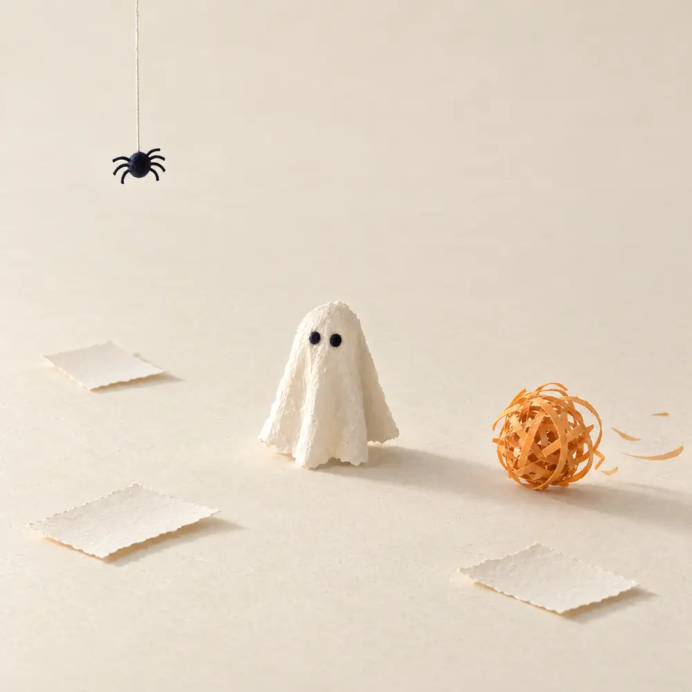 Een klein papieren spookje alleen tussen lege kaartjes, met een tumbleweed die voorbijrolt en een spin die erboven hangt